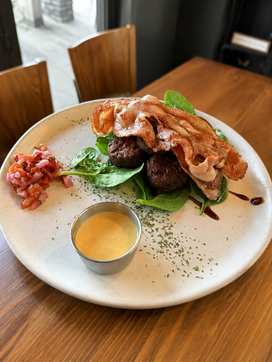 A breakfast plate with bacon, sausage and greens at Nourish Cafe